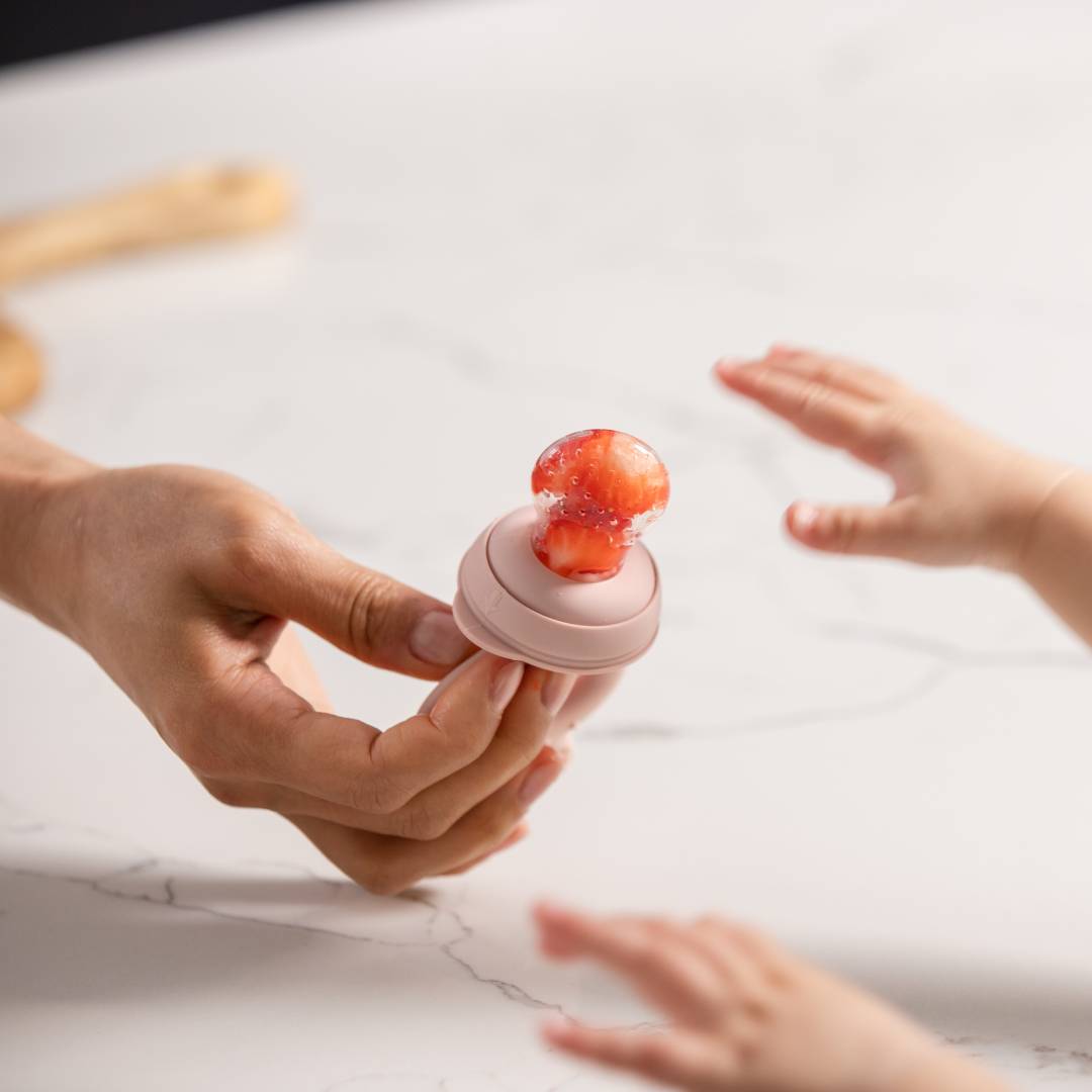 A mother hands her child a Haakaa Fresh Food Feeder with fresh strawberries in the pouch