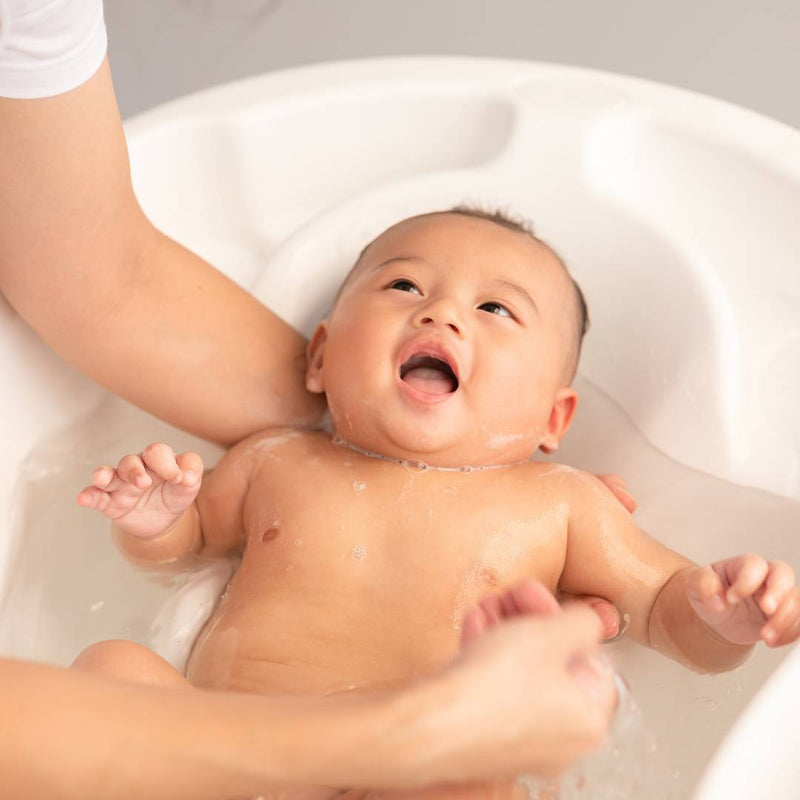 Smiling newborn baby being bathed in a dedicated baby bath