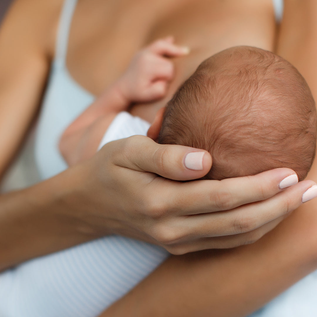 A mother's hand cradling her newborn baby's head as they breastfeed